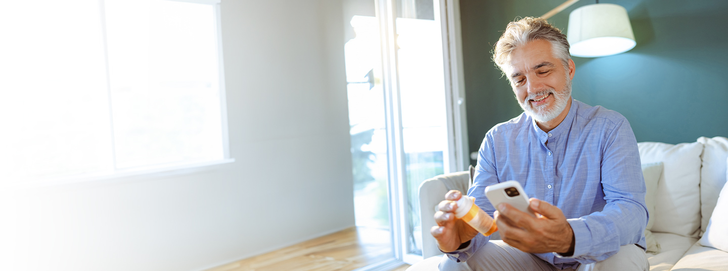 Bearded man sitting down looking at cellphone and holding prescription medicine bottle